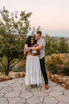 a man and woman hugging each other in front of an apple tree