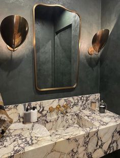 a bathroom with marble counter tops and gold fixtures on the wall, along with two round mirrors