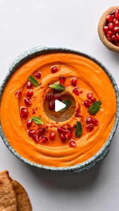 a bowl filled with carrot hummus and topped with pomegranates next to crackers