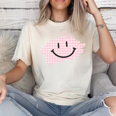 Comfort Colors Smiley Face Plaid T-Shirt | Cute and Cozy Design Stay comfy and cute with this fun Comfort Colors 1717 t-shirt featuring an adorable smiley face peeking out from a trendy plaid design! Crafted from ultra-soft, vintage-washed cotton, this tee is perfect for anyone who loves laid-back style with a playful twist. The unique blend of classic plaid and a happy, smiling face brings a little extra joy to your everyday wardrobe. Features: -Comfort Colors 1717 Tee: Made from 100% ring-spun cotton for that lived-in softness from day one. -Playful Design: The cute smiley face peeking out from a plaid pattern adds charm and personality to your outfit. -Relaxed Fit: Ideal for casual, everyday wear with its relaxed and comfortable silhouette. -Versatile Style: Dress it up with your favori Casual Plaid Cotton T-shirt, Cotton Gingham Tops For Everyday, Cute Plaid Short Sleeve Tops, Cute Short Sleeve Plaid Tops, Cute Cotton Tops With Smiley Face, Cute Tops With Funny Print For Everyday, Playful White Top With Smiley Face, Cute Pink Smiley Face Top, White Playful T-shirt With Smiley Face