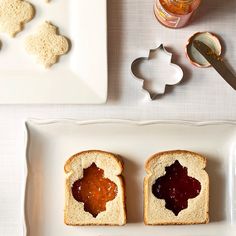 four pieces of bread with jam on them sitting on a white plate next to utensils