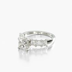 a white gold ring with three princess cut diamonds on the sides and side stones at the top