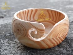 a wooden bowl sitting on top of a stone floor next to a cup with a spiral design