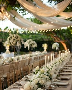 a long table is set with white flowers and candles for an elegant wedding reception in the garden