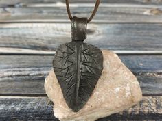 a leaf shaped pendant sitting on top of a piece of wood next to a rock