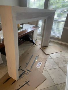 an unfinished table is sitting on the floor in front of a window with shutters