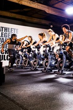 a group of people riding stationary bikes in a gym with an advertisement on the wall behind them