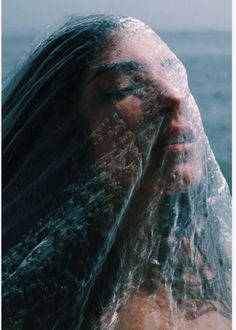 a woman covered in plastic covering her face and head with the ocean in the background