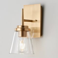 a wall light with a glass shade on it's side and a gold finish