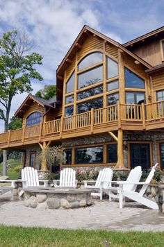 two white lawn chairs sitting in front of a large wooden house on a sunny day