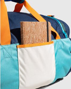 a blue and white duffel bag with a wooden pocket in the front that has a notepad sticking out of it