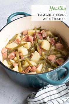 a pot filled with green beans and potatoes on top of a white counter next to a towel