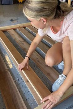 a woman kneeling down on top of a wooden floor next to a metal frame and plywood planks