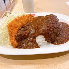 a white plate topped with meat covered in gravy next to rice and cole slaw