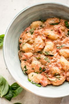 a white bowl filled with pasta and spinach on top of a marble countertop