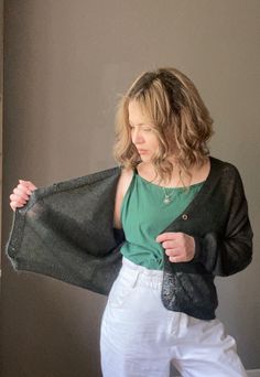 a woman in white pants and a green shirt is holding a black jacket over her shoulder