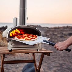 a pizza is being cooked in an outdoor oven on a wooden table near the beach