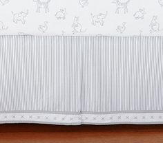 a bed skirt with animals on it and white trim around the edges, in front of a wooden floor