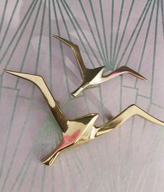 two gold bird brooches sitting on top of a pink and green table cloth