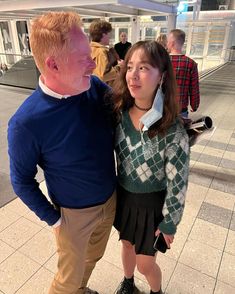 a man and woman standing next to each other in front of a train station platform