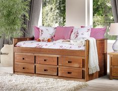 a wooden bed with drawers underneath it in a living room next to a large window