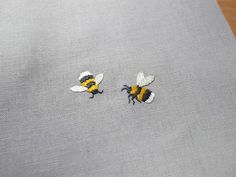 two small embroidered bees sitting on top of a piece of cloth next to each other