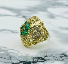 Beautiful Gold Color Filigree Flower Ring with Emerald Green and Zircon Subtleties This stunning ornate gold color filigree ring will dazzle her with it's lovely floral design, round brilliant cut zircon stone accents, and a glorious cluster of nine rich emerald green stones set in 925K silver The intricate filigree work is the ultimate symbol of elegance and glamour,  giving you a perfect choice for all occasions. Material: Silver Stones : Green Emerald white Stone Design: Fine work of floral f Gold Emerald Ring With Intricate Heirloom Design, Gold Emerald Heirloom Ring With Intricate Design, Gold Emerald Ring With Intricate Design For Gift, Gold Emerald Ring With Intricate Design, Oval Shape, Oval Gold Emerald Ring With Intricate Design, Ornate Gold Filigree Ring With Gemstone, Gold Filigree Ring With Accent Stones For Anniversary, Anniversary Gold Filigree Ring With Accent Stones, Gold Filigree Ring With Gemstone