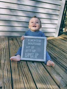 a baby sitting on the ground holding up a sign