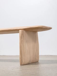 a wooden bench sitting on top of a cement floor next to a white wall in an empty room