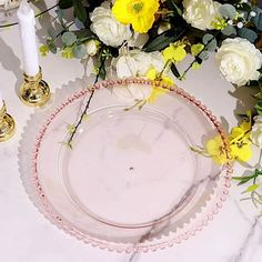 a table topped with a glass plate covered in yellow and white flowers next to candles