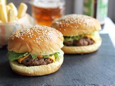 two hamburgers with cheese and lettuce are on a table next to fries