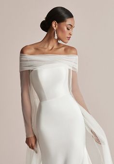 a woman in a white wedding dress with an off the shoulder cape