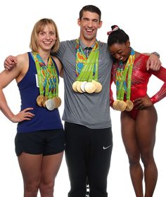 three people standing next to each other with medals on their heads and arms around them