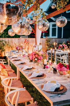 a long table set up for a party with pink flowers and disco balls hanging from the ceiling