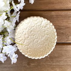 a white plate sitting on top of a wooden table next to some white flowers and greenery