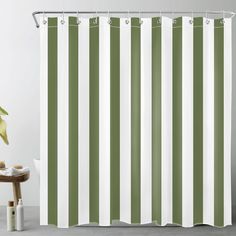 a green and white striped shower curtain next to a table with a potted plant