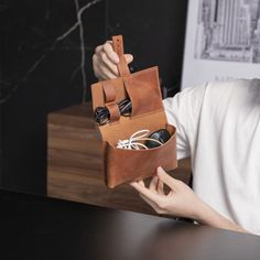 a man holding a brown leather case with earbuds in it's pocket