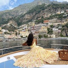 a woman sitting on the back of a boat in front of a city and mountains