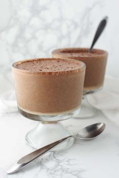 two glasses filled with chocolate pudding on top of a marble countertop next to spoons