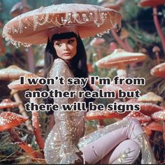 a woman sitting on the ground in front of mushrooms with an umbrella over her head