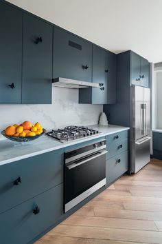 a kitchen with blue cabinets and white countertops has oranges in a bowl on the stove