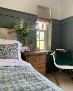 a bed sitting next to a window with a green blanket on top of it and a white chair in front of it