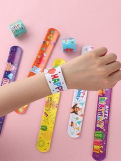 a person's hand holding onto an assortment of colorful wristbands on a pink background