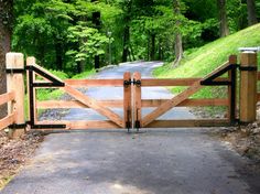 a wooden gate is open on the side of a road in front of some trees