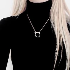 a woman with blonde hair wearing a black shirt and silver necklace, standing in front of a white background