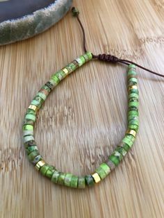 a green beaded bracelet sitting on top of a wooden table