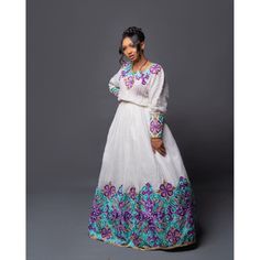 This Habesha Kemis is a true masterpiece of Ethiopian fashion, crafted with the finest Menen fabric and adorned with a stunning Tilf pattern that is sure to turn heads. The intricate details of the pattern, including the vibrant purple and blue colors and delicate shapes, are expertly woven into the fabric, creating a stunning visual effect that is both bold and regal. The dress itself is a Shimena style, designed to be form-fitting and flattering to the wearer's figure. The dress hugs the curve Bollywood Style Maxi Dress For Traditional Ceremonies, Traditional Multicolor Long Sleeve Gown, Traditional Long Sleeve Multicolor Gown, Transitional Long Sleeve Maxi Dress, Long Sleeve Dresses With Dabka For Transitional Season, White Long Sleeve Maxi Dress For Navratri, Transitional Season Multicolor Gown, Fitted Long Sleeve Maxi Dress For Transitional Season, Multicolor Long Sleeve Embroidered Dress For Wedding