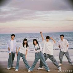 four people standing on the beach with their arms in the air and one person holding his hand up