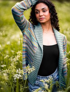 a woman is standing in the grass with her arms behind her head and looking at the camera