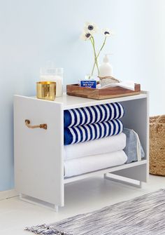 a white cabinet with blue and white striped towels on it's shelf next to a vase